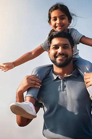 Père souriant portant sa fille sur ses épaules à bras ouverts.