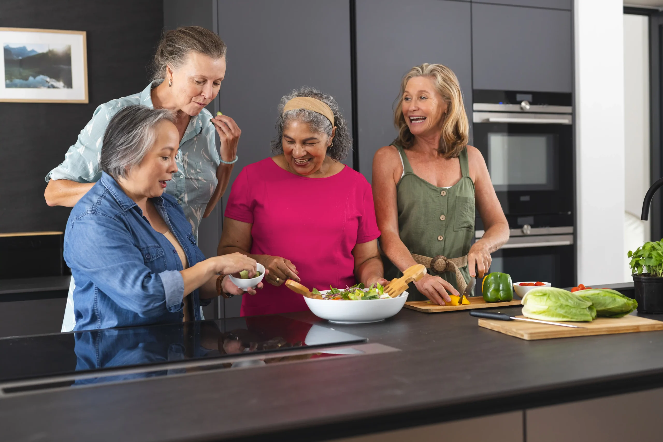 Au Centre femmes de La Mitis-Mission inclusion Quatre amies âgées préparent une salade ensemble dans une cuisine moderne et lumineuse, profitant d'un moment convivial