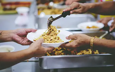 Une personne servant une assiette de pâtes à une autre.