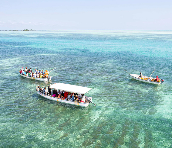 ReSea. Petits bateaux transportant des visiteurs sur une eau turquoise transparente dans une zone côtière tropicale.